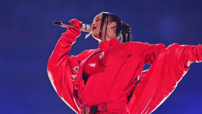 Rhianna sings in a monochrome red outfit with a navy background (Image from MSNBC)