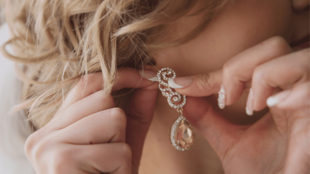 An ear with female hands putting on dangle earrings