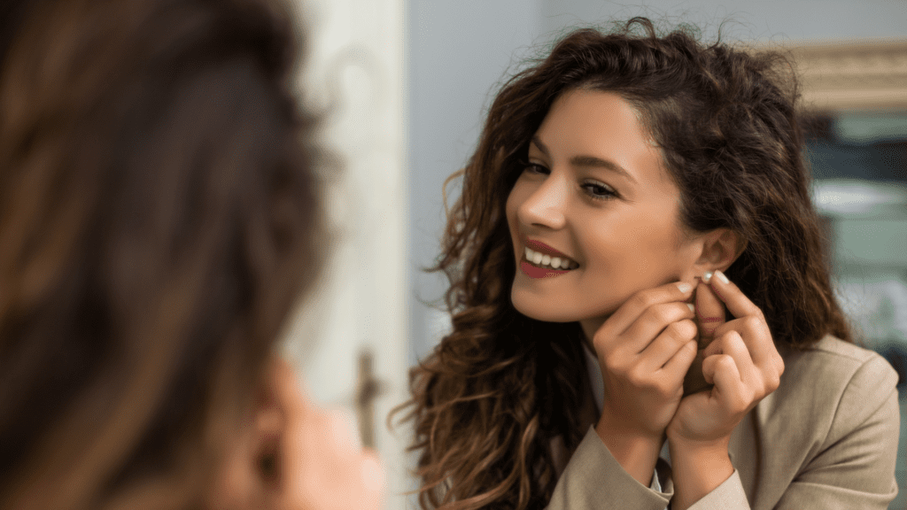 Woman looking in the mirror while putting on earrings