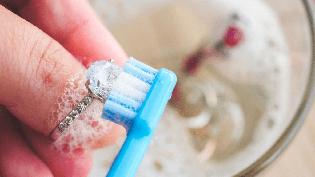 Cleaning a diamond ring in soapy water with a toothbrush.