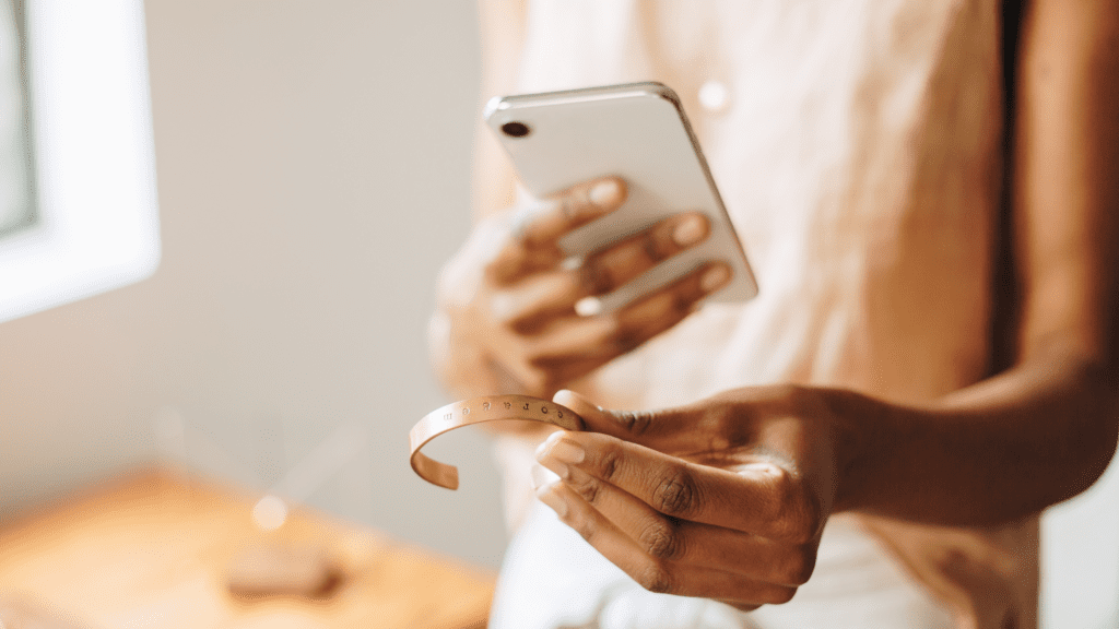 A hand holding a bracelet while the other holds a phone as if to take a picture.