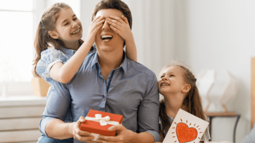 two little girls surprising dad with a gift.
