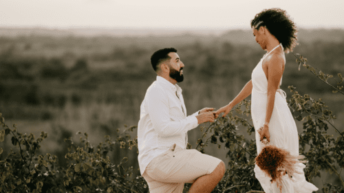 A man on one knee presenting an engagement ring to a woman.