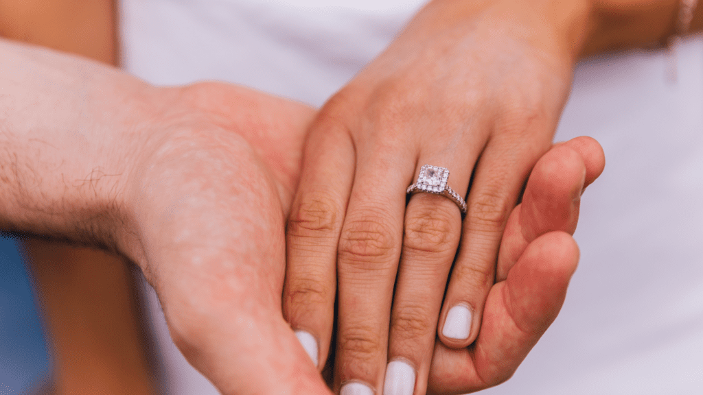 A couple's embraced hands, displaying the diamond engagement ring.
