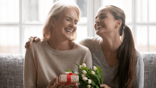 Mom and daughter smiling together, daughter is giving her mother gifts.